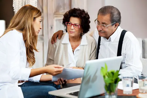 Young woman consulting elderly couple with documents and laptop.