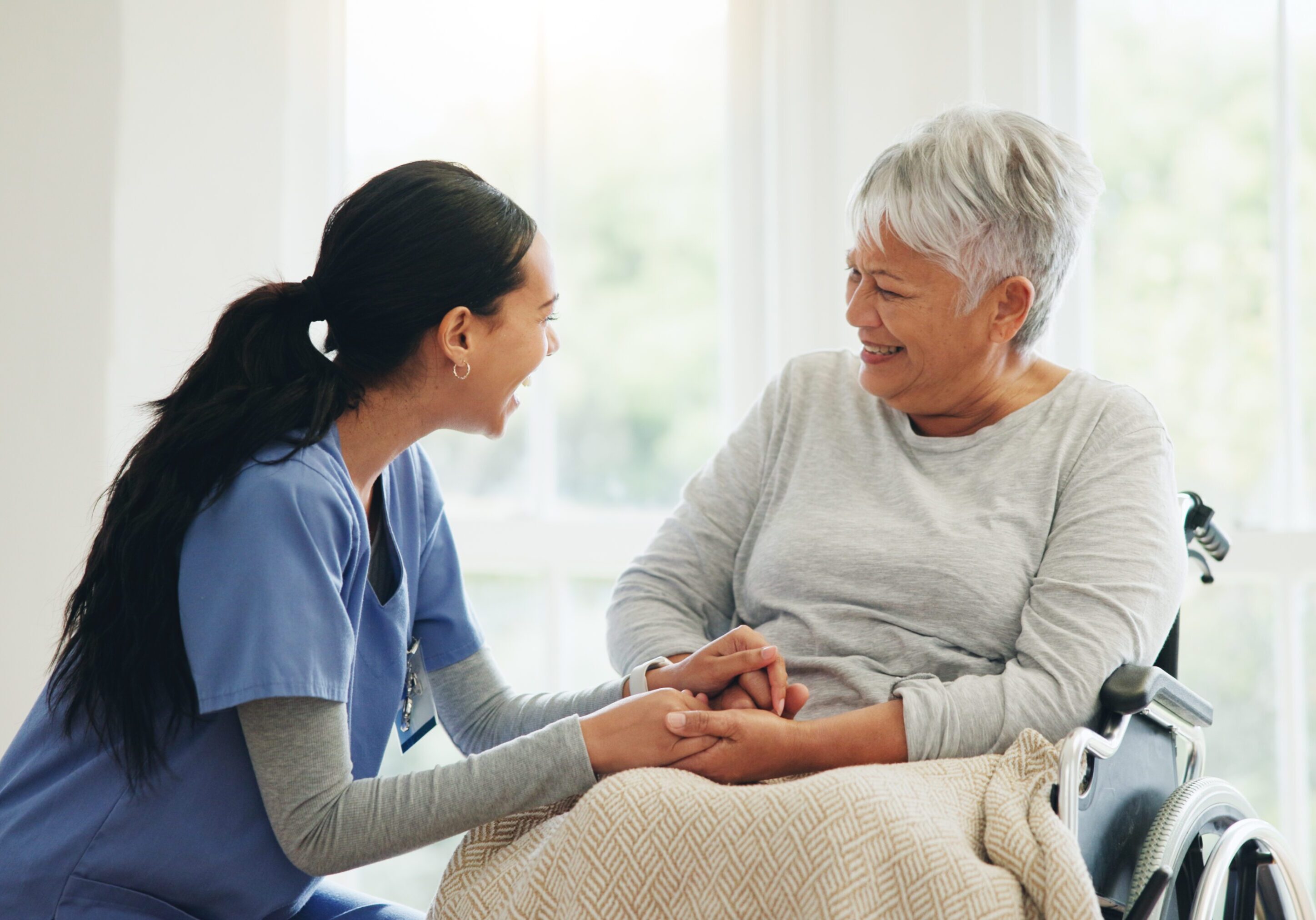 A nurse warmly holding hands with an elderly woman.